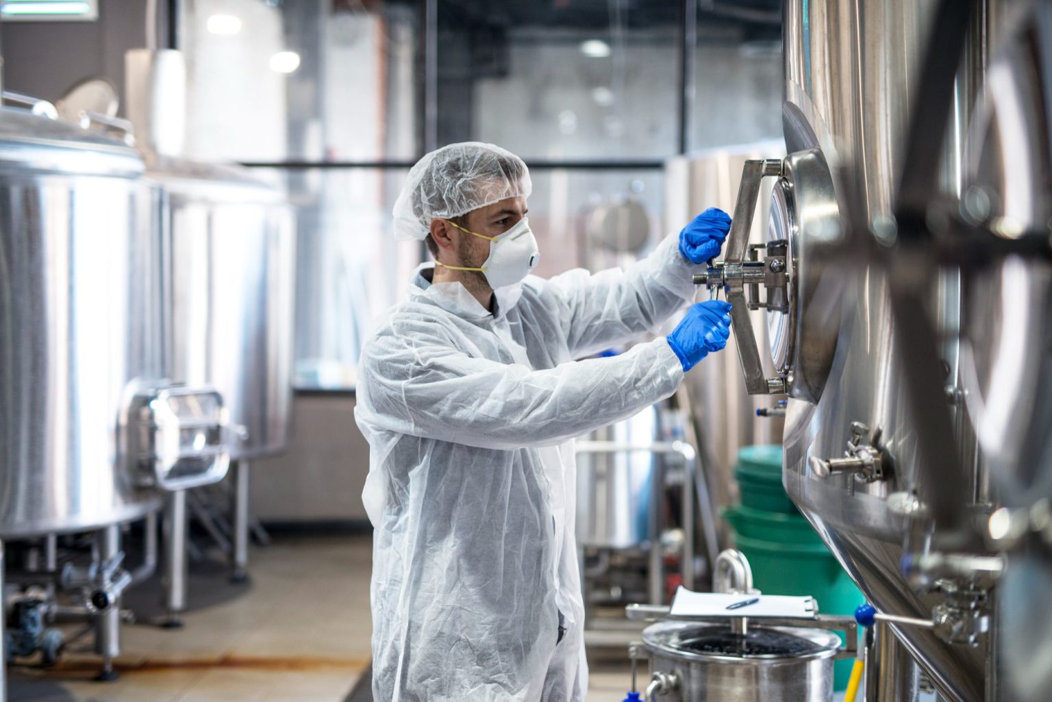 technologist-protective-uniform-wearing-hairnet-mask-goggles-gloves-closing-industrial-tank-reservoir-min-1536×1025-1